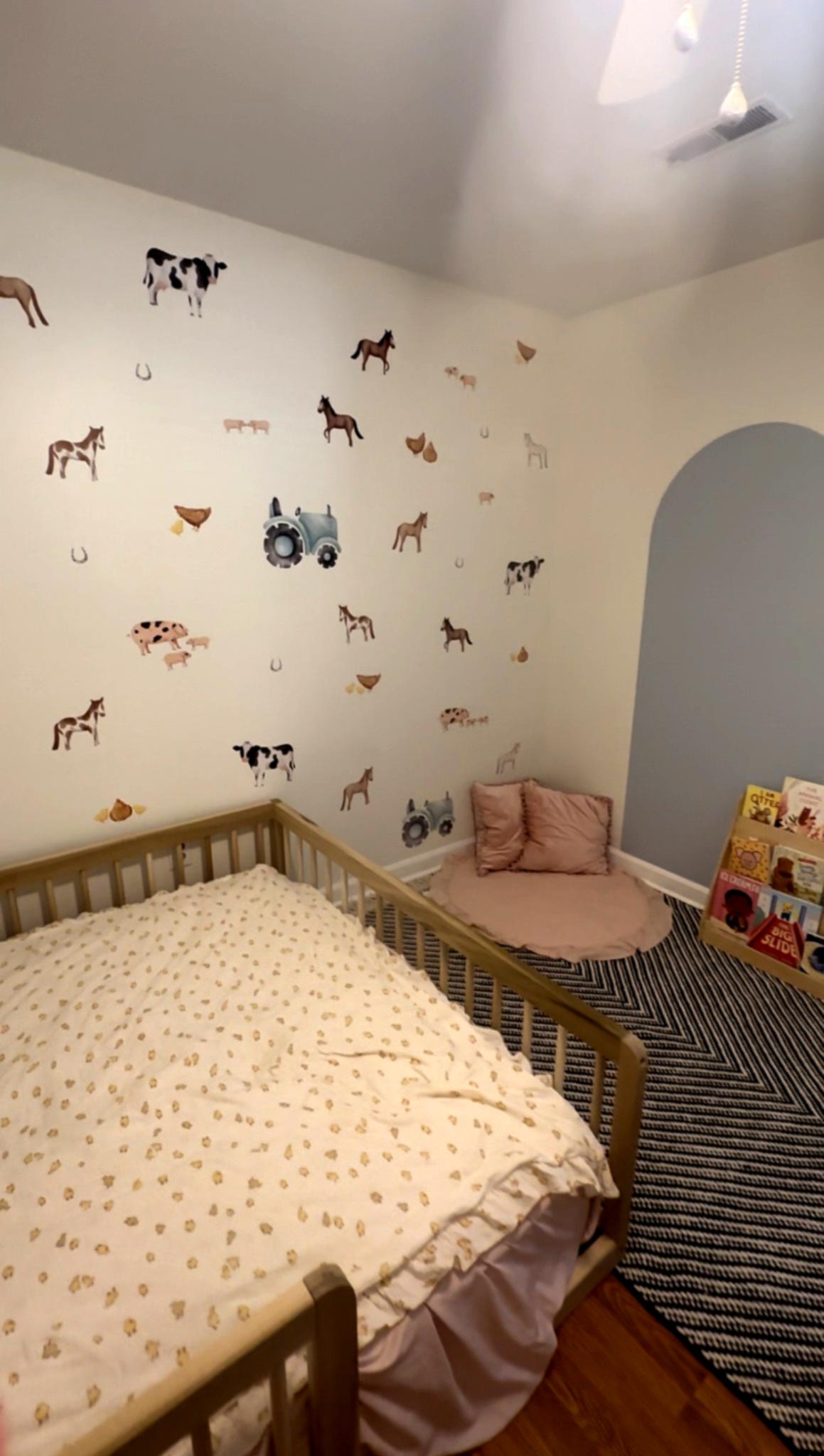 Nursery room corner with a toddler bed, featuring farm animal-themed wallpaper and a cozy reading nook. The wall is decorated with horse, cow, and chicken decals, complemented by a soft pink floor pillow