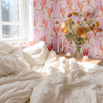 Bright and airy bedroom with boho-inspired decor, heartland cactus wallpaper, white bedding, and a vase of fresh flowers