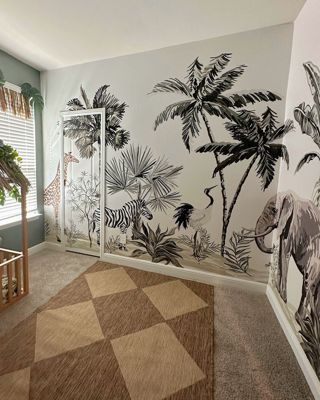 Safari-themed nursery room with a mural featuring zebras, giraffes, palm trees, and elephants. Natural wood crib with tropical bedding and leafy decorations. A cozy, playful space for a child