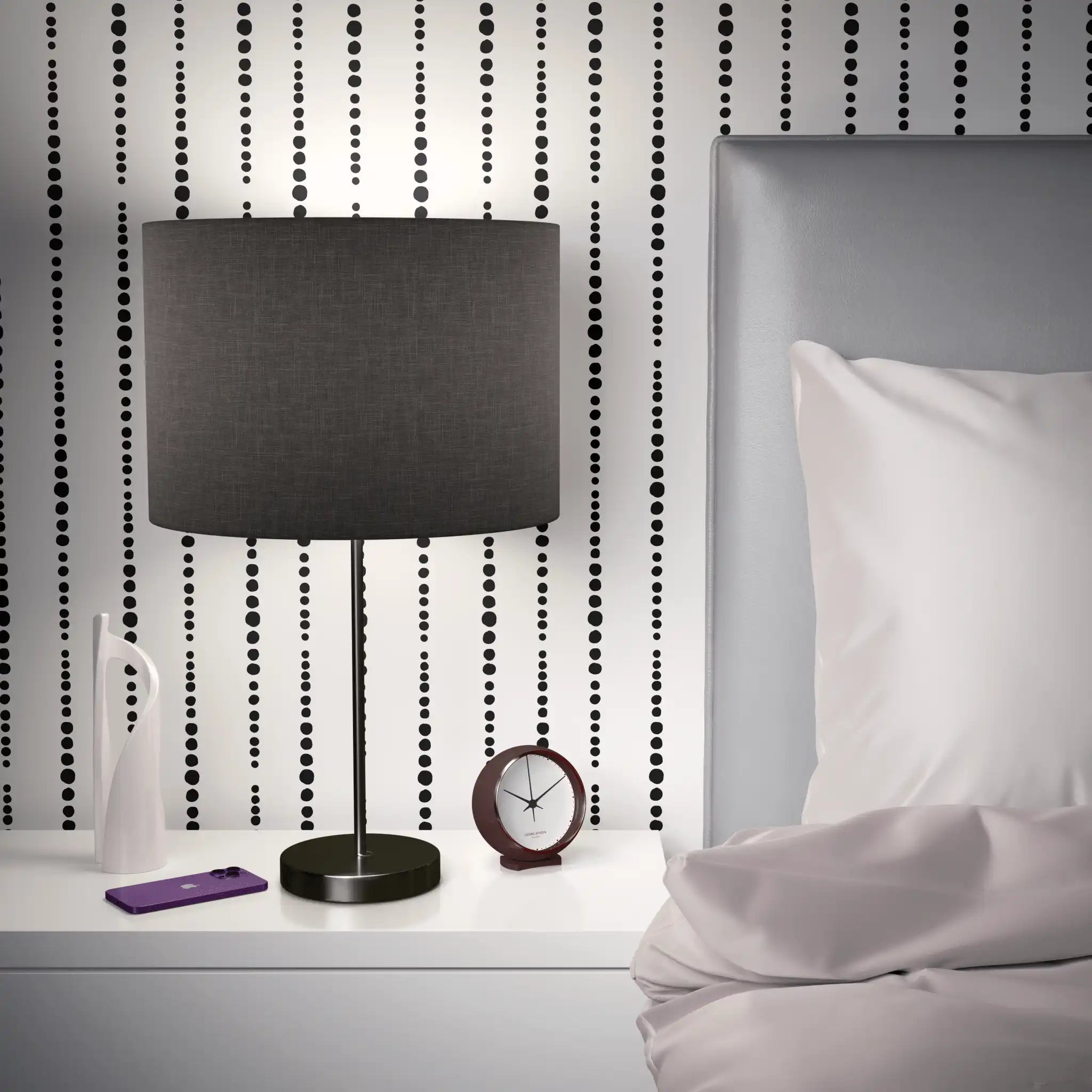Modern black and white dot wallpaper behind bedside lamp and grey headboard