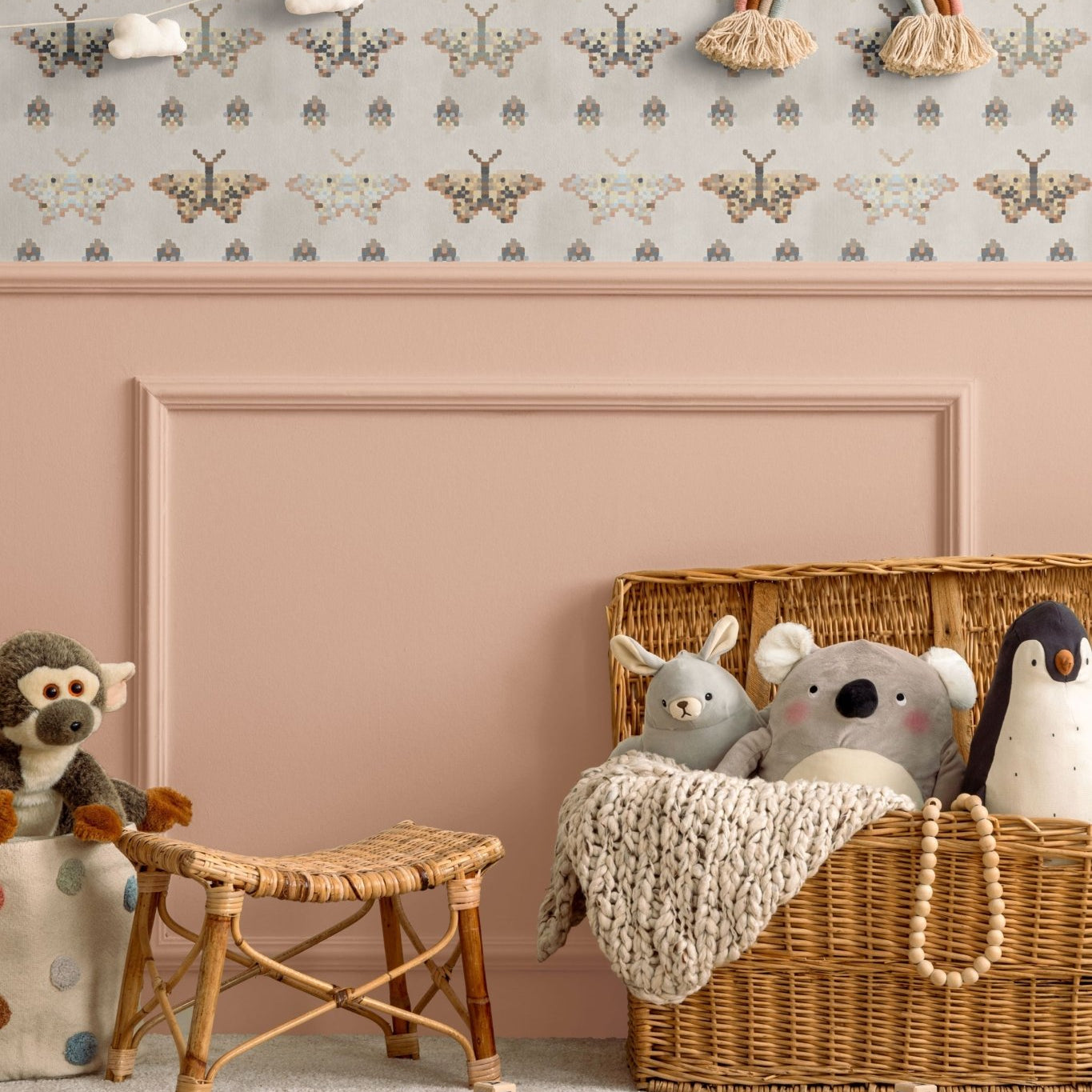 Cozy children's room with mosaic butterfly wallpaper in pastel and earthy tones. The room features a wicker toy basket with plush animals, a rattan stool, and a pink wall with a rainbow decoration and cloud garland, creating a warm, playful space