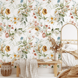 A cozy bedroom corner with a floral watercolor wallpaper, showcasing a bench with a cream throw blanket and a woven basket.