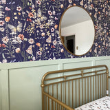  A charming nursery featuring a navy blue wallpaper adorned with detailed floral and butterfly patterns, complemented by a circular mirror and a green half-wall.