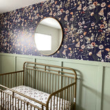 Nursery displaying the entire brass crib, navy blue butterfly wallpaper, and the reflective circular mirror mounted above