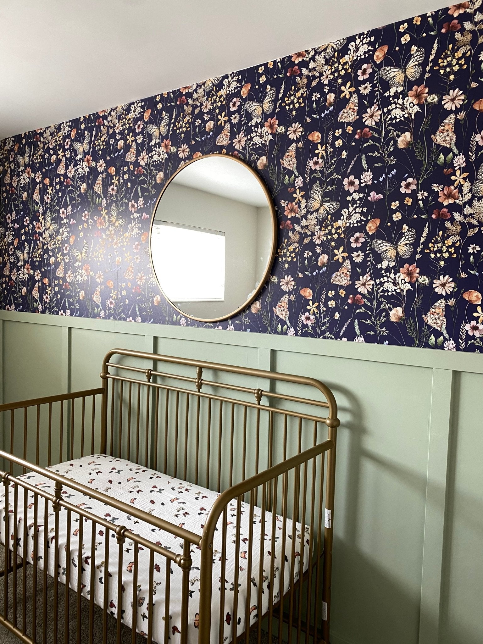 Nursery displaying the entire brass crib, navy blue butterfly wallpaper, and the reflective circular mirror mounted above