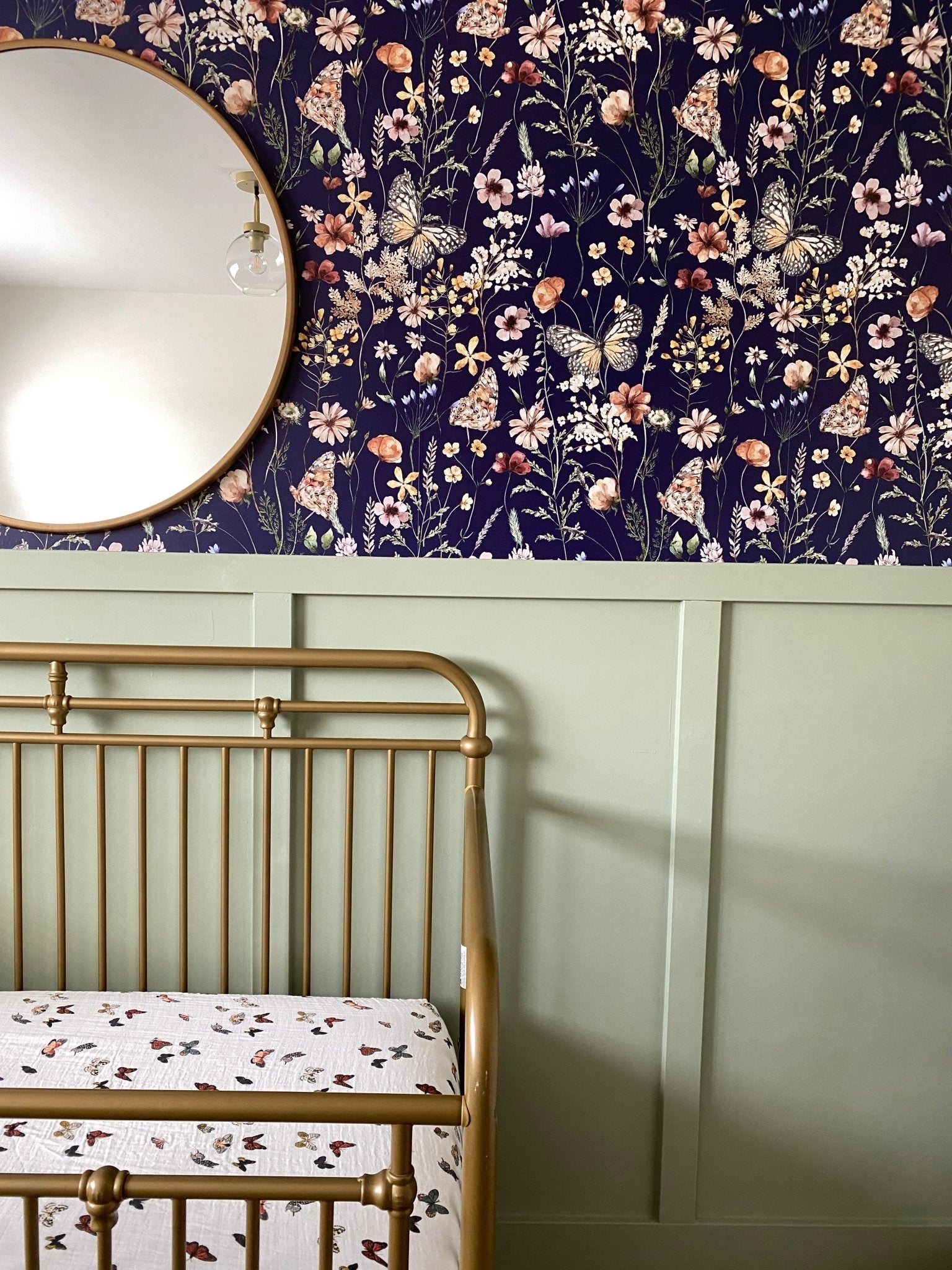 Close-up of the nursery showing the same navy blue butterfly-themed wallpaper and the top of a brass crib against a green half-wall