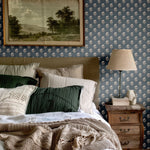 Classic bedroom setup with navy blue floral wallpaper, green and beige pillows, and a rustic wooden nightstand