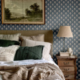 Classic bedroom setup with navy blue floral wallpaper, green and beige pillows, and a rustic wooden nightstand