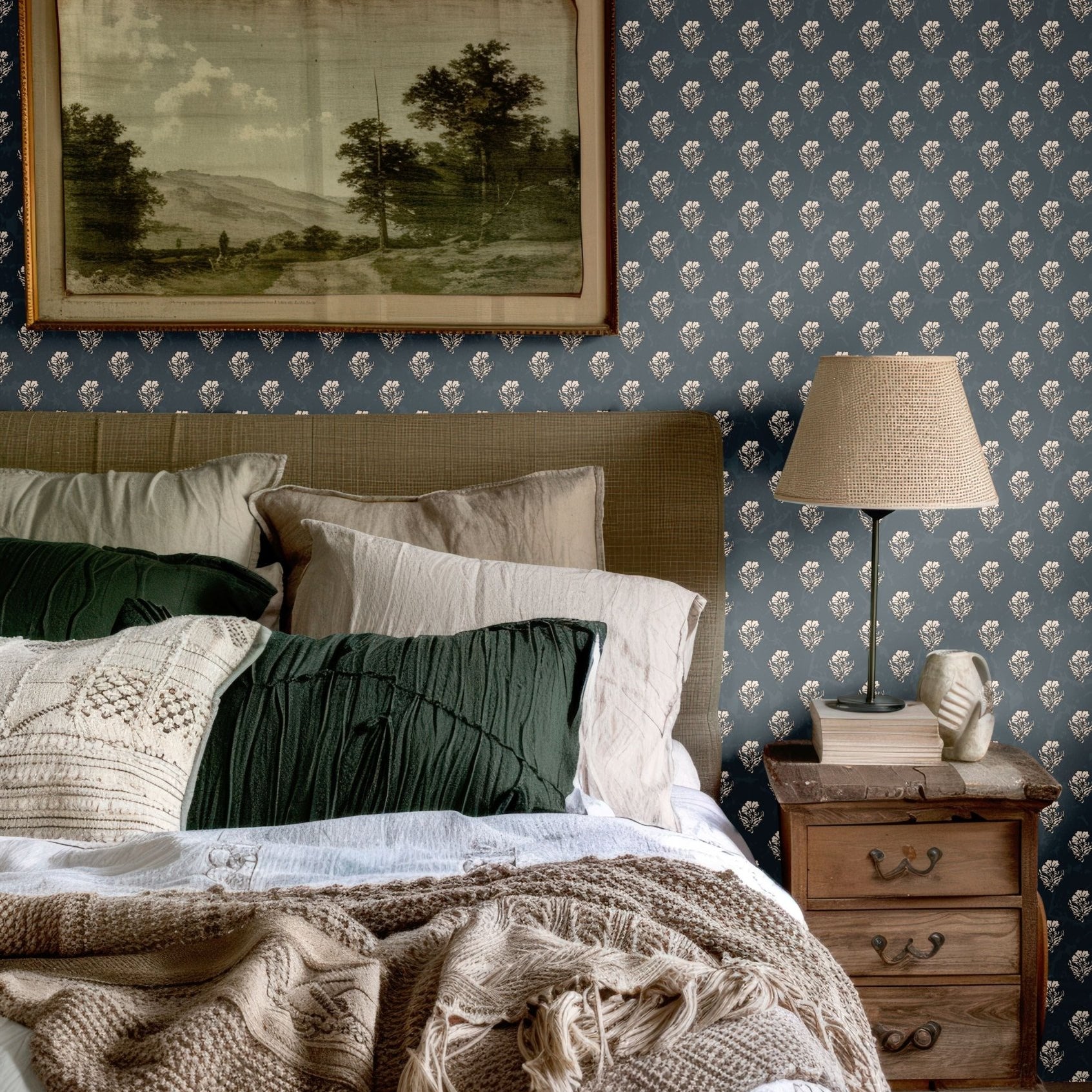 Classic bedroom setup with navy blue floral wallpaper, green and beige pillows, and a rustic wooden nightstand