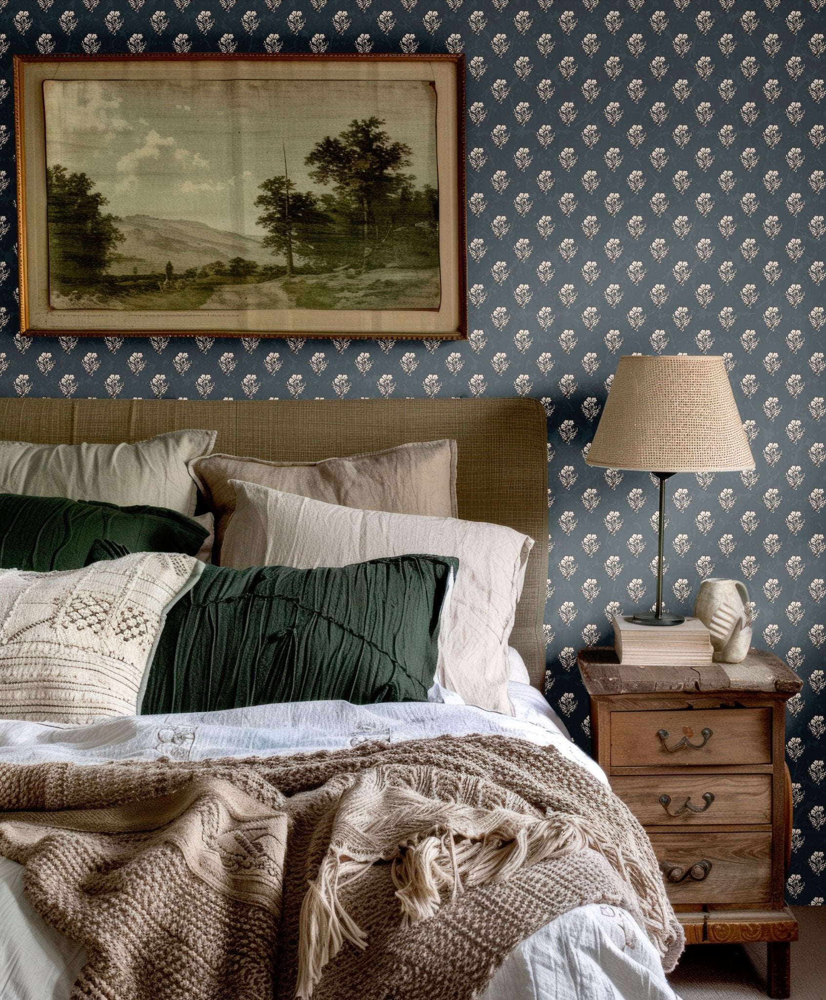 Classic bedroom setup with navy blue floral wallpaper, green and beige pillows, and a rustic wooden nightstand