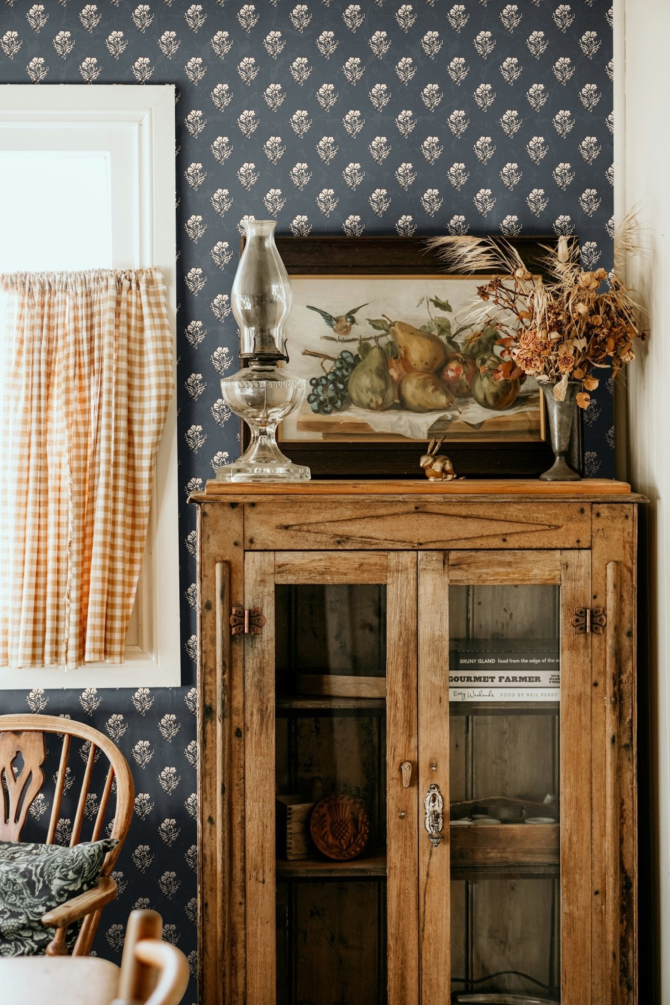 Vintage kitchen corner with navy blue floral wallpaper, an antique wooden cabinet, and decorative rustic elements