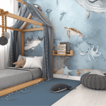 Cozy boy's bedroom with a canopy bed and an expansive undersea wall mural. The mural depicts lifelike illustrations of marine life such as a hammerhead shark, jellyfish, sea turtle, and a playful octopus. The bed is adorned with a grey bedspread, starry grey canopy, and a cushioned pouf nearby, creating an inviting ocean-themed nursery atmosphere