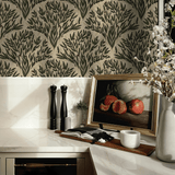 A stylish kitchen corner showcasing olive branch wallpaper as a backdrop. The scene includes marble countertops, a vase with blooming branches, salt and pepper mills, and an artwork of pomegranates.