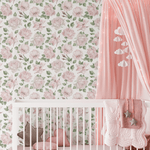 A cozy nursery room with a white crib adorned with a pink star pillow and a heart-shaped pillow, set against a wall covered in pink rose-patterned wallpaper. A pink canopy with cloud-shaped decorations hangs over the crib, adding a dreamy touch to the room.