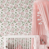 Close-up view of a charming nursery with a white crib, pink and gray star-shaped pillows, and a pink canopy with cloud-shaped decorations. The backdrop features a pink rose-patterned wallpaper, creating a serene and whimsical atmosphere.