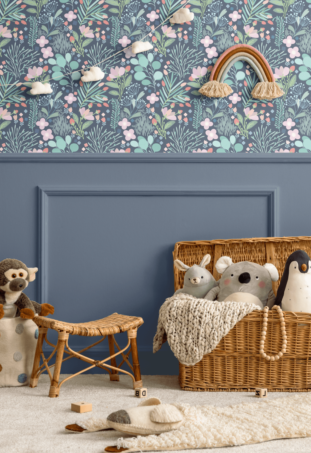 Nursery room with blue floral wallpaper featuring pastel-colored flowers and leaves on the upper half of the wall, a blue wainscoting panel below, and wicker baskets and stuffed animals as decor elements
