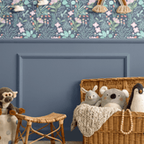 Nursery room with blue floral wallpaper featuring pastel-colored flowers and leaves on the upper half of the wall, a blue wainscoting panel below, and wicker baskets and stuffed animals as decor elements