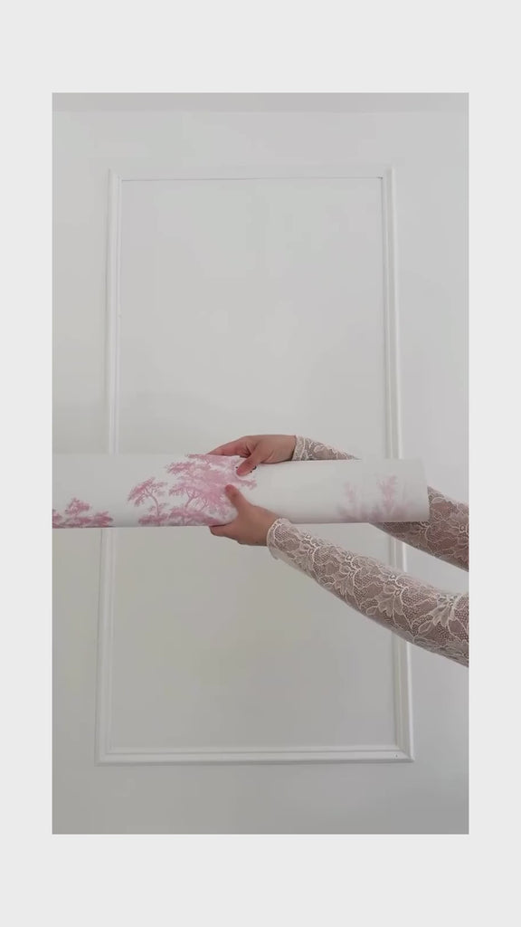 Unrolling pink toile wallpaper with ballerinas, trees in the background.
