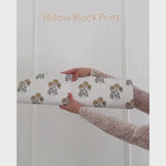 Unrolling cream coloured wallpaper with yellow flowers, charcoal grey stems.