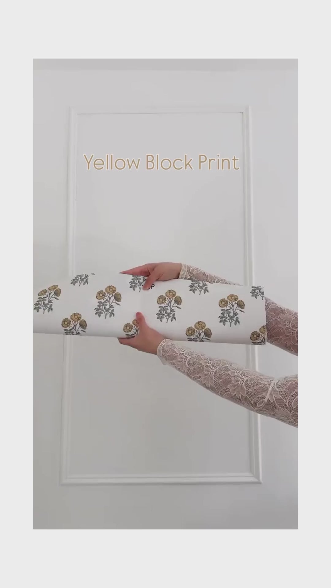 Unrolling cream coloured wallpaper with yellow flowers, charcoal grey stems.