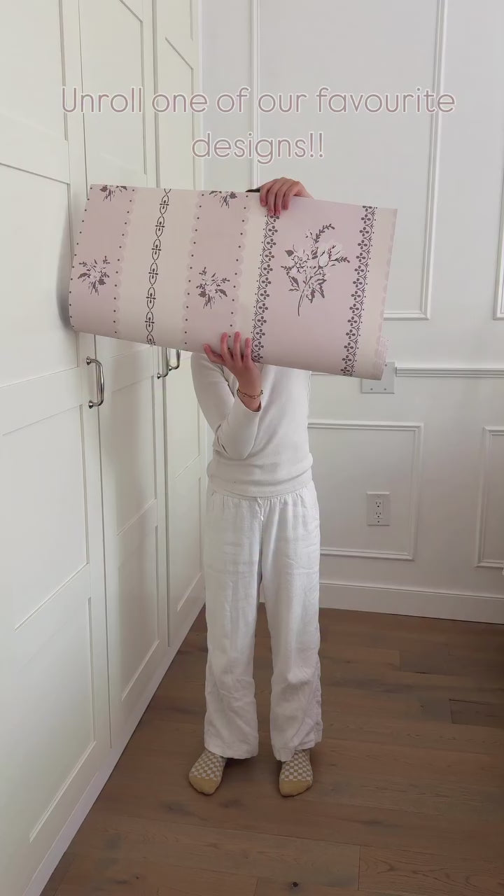 Unrolling the pink vertical stripe wallpaper with dainty black print. 