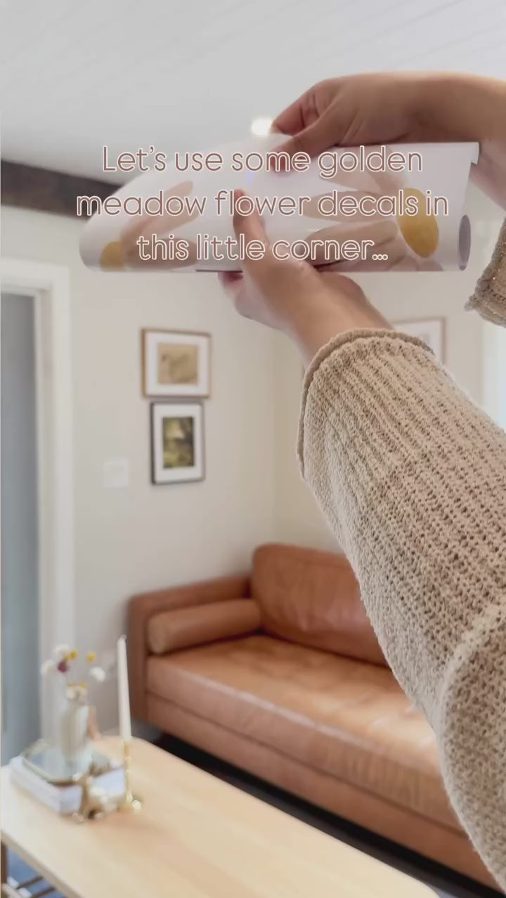 Let's use some golden meadow flower decals in this corner... video shows unrolling daisy decals and placing them on a wall. Styled with a brown leather couch. Very beautiful! 