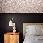 Romantic floral wallpaper above black wainscoting in cozy modern bedroom with wood nightstand and neutral bedding