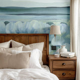 Abstract blue and green wall mural featured above a rustic wooden bed with beige linens.