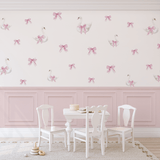 Swan and bow decals on a white wall with pink paneling in a girls' playroom with a white table and chairs.