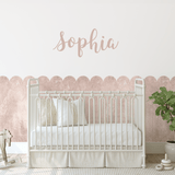 A pink limewash scallop border accentuating a white nursery with an elegant name decal above the crib.