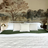 A serene bedroom featuring a Vintage Landscape mural with a tree dominating the scene, flanked by gold lamps and crisp white bedding with a green accent.