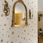 A closer view of the beige floral wallpaper, showing its texture and the gold-framed mirror and sconces on the wall. A light switch is visible on the right.