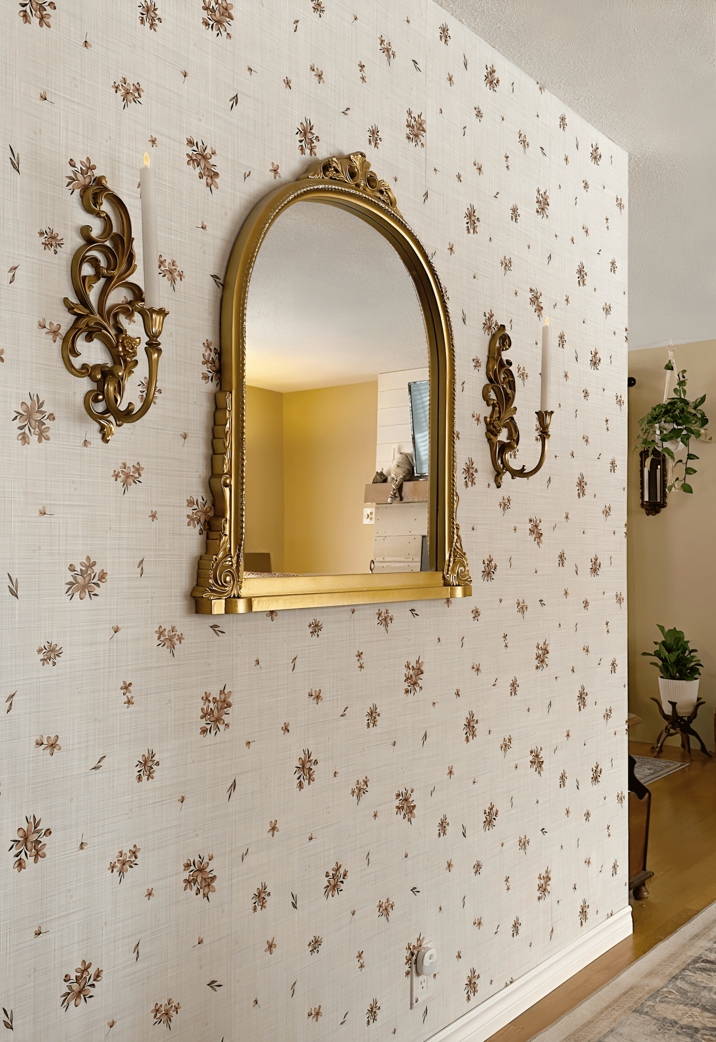 A closer view of the beige floral wallpaper, showing its texture and the gold-framed mirror and sconces on the wall. A light switch is visible on the right.