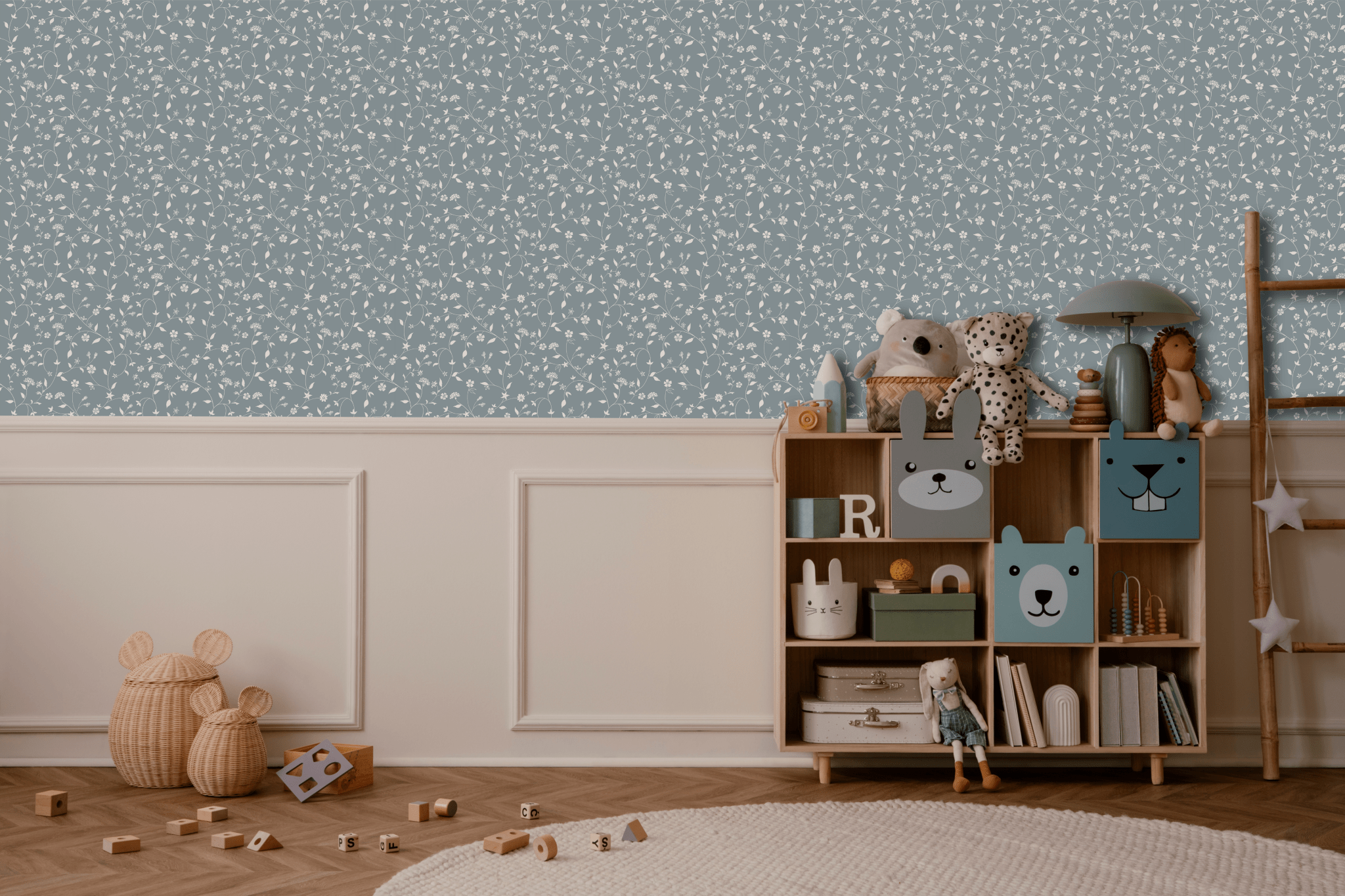 A charming boy's room with blue vine patterned removable wallpaper. A wooden toy shelf is filled with cute animal figures, plush toys, and books. A woven basket and scattered blocks on the floor add a playful touch