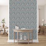 A tasteful room featuring blue vintage peel and stick removable wallpaper with a floral pattern. A wooden table with decorative pieces is set against the wallpaper, and a peek into the adjoining dining area reveals a sideboard and potted plant