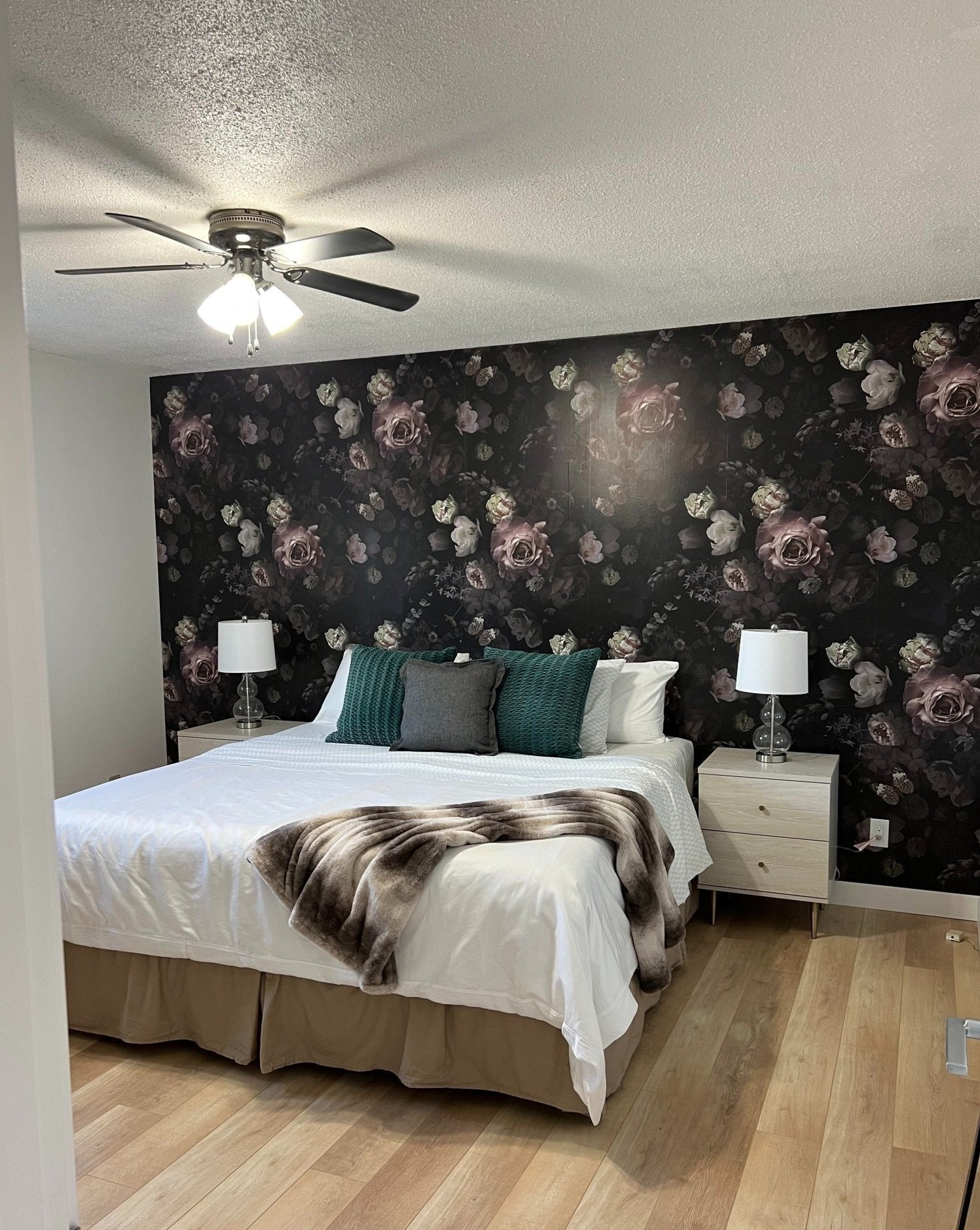 Moody Dark Floral wallpaper in a room with ceiling fan, white bedding, and light wood flooring