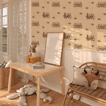 A child's room with whimsical duck-patterned wallpaper, a wooden table, books, a music box, a wicker chair with a deer cushion, and plush toys