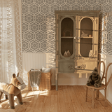 A cozy children's room corner featuring a playful rocking horse, a wicker basket with a knit throw and cushion, and a vintage-style wooden cabinet against a wall adorned with black and white hexagon pattern wallpaper
