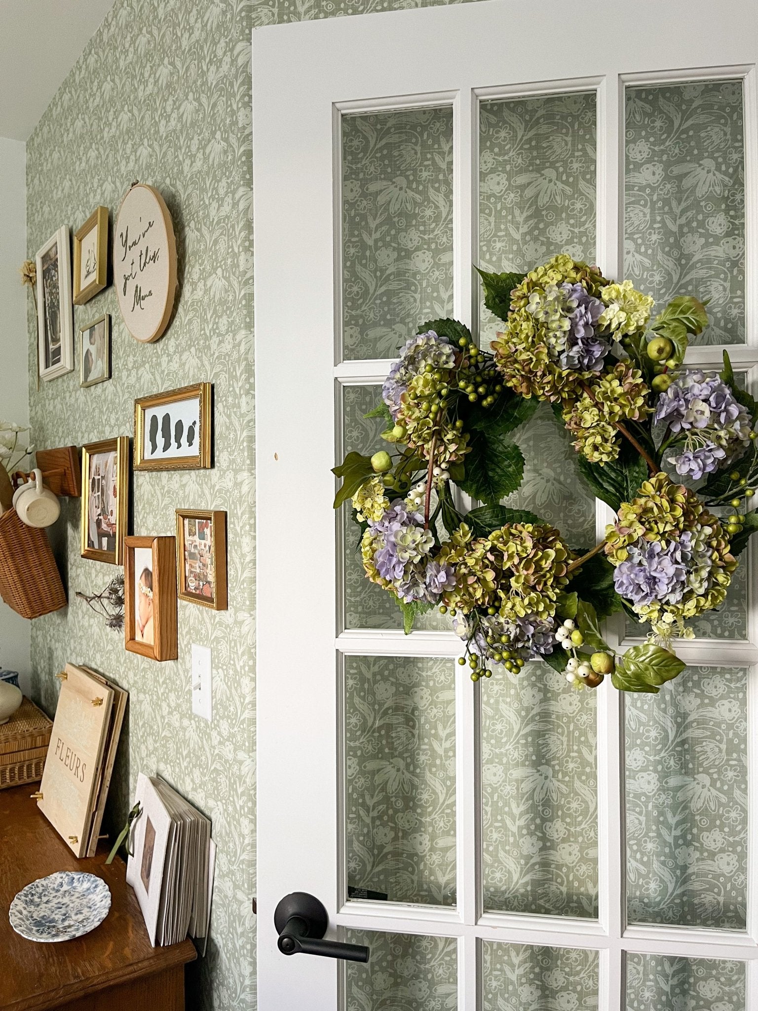 Sage dainty floral wallpaper on an office wall with vintage picture frames and beautiful floral wreath.