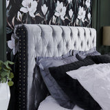 A close-up of a bedroom showing a wallpaper with white magnolias on a black background, matching the gray tufted headboard with black accents.