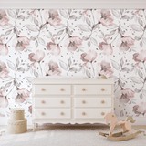 Nursery room with large blush floral wallpaper, white dresser with peach knobs, wooden rocking horse, and scalloped yellow storage.