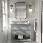 A light-filled bathroom with pastel floral peel and stick wallpaper, a blue vanity, and a pink rug on marble flooring