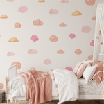 Interior of a girl's bedroom featuring walls with pink and orange watercolor cloud stickers, a cozy bed with pink bedding, and a white canopy with fairy lights