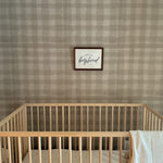 Minimalist nursery with a wooden crib, stuffed toy, and wall art reading "long live boyhood" against plaid wallpaper.