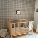 Airy baby room with crib, white blanket, toys, "long live boyhood" frame, rattan light, and gingham wallpaper.