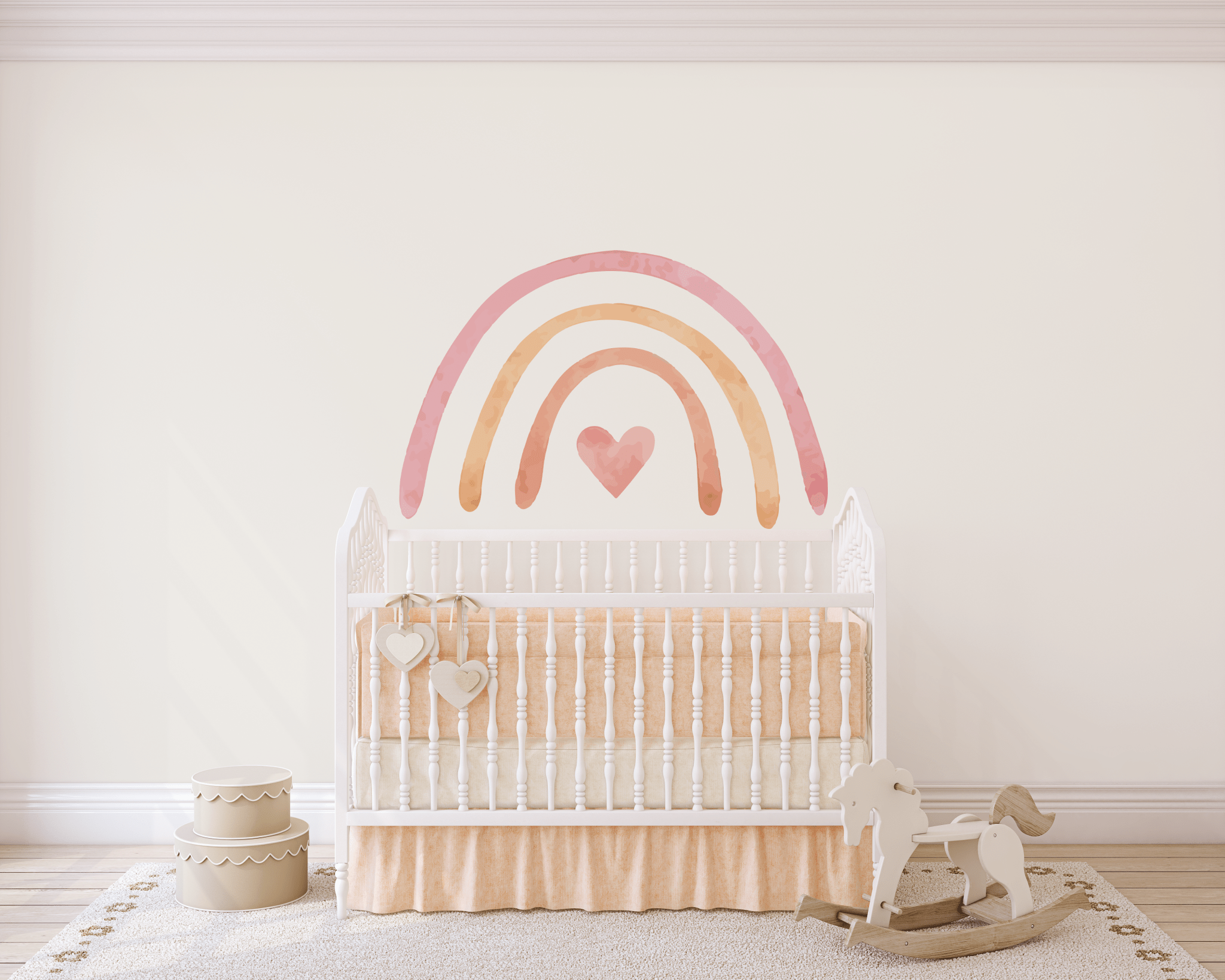 A nursery with a large pastel rainbow wall sticker positioned above a classic white crib. The crib has a beige blanket, and nearby is a white rocking horse toy. The floor is adorned with a soft rug and there's a pair of decorative white hearts hanging on the crib.