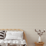 A warm and inviting bedroom showcasing white-washed rattan weave wallpaper, a rattan bed frame with striped bedding, and a vase of cotton stems on a woven bedside stool.