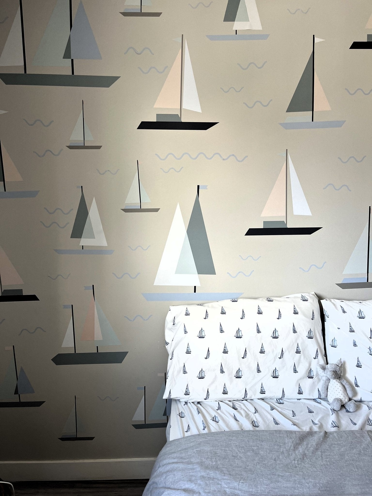 A bedroom with a wall covered in sailboat decals, complementing bedding with a similar pattern, and a plush toy on the bed, creating a serene nautical theme.