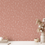 A close-up of a wall covered in terracotta-colored removable wallpaper with a botanical print, beside a desk with minimalistic decor and a productivity planner.