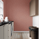 A modern laundry room with a bold terracotta dainty floral wallpaper, contrasting with white cabinets, black countertops, and wicker laundry baskets.